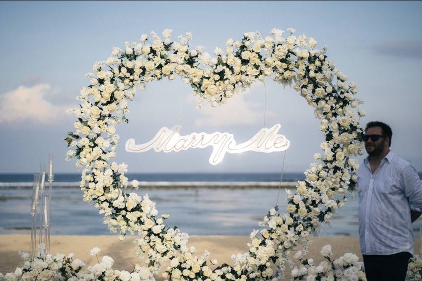 The Marry Me sign inside a heart of white roses on the beach
